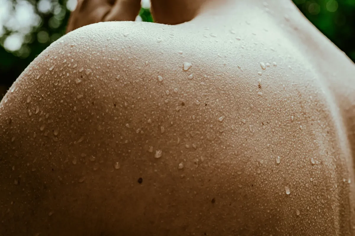 Wassertropfen auf einer Schulter, umgeben von Grün
